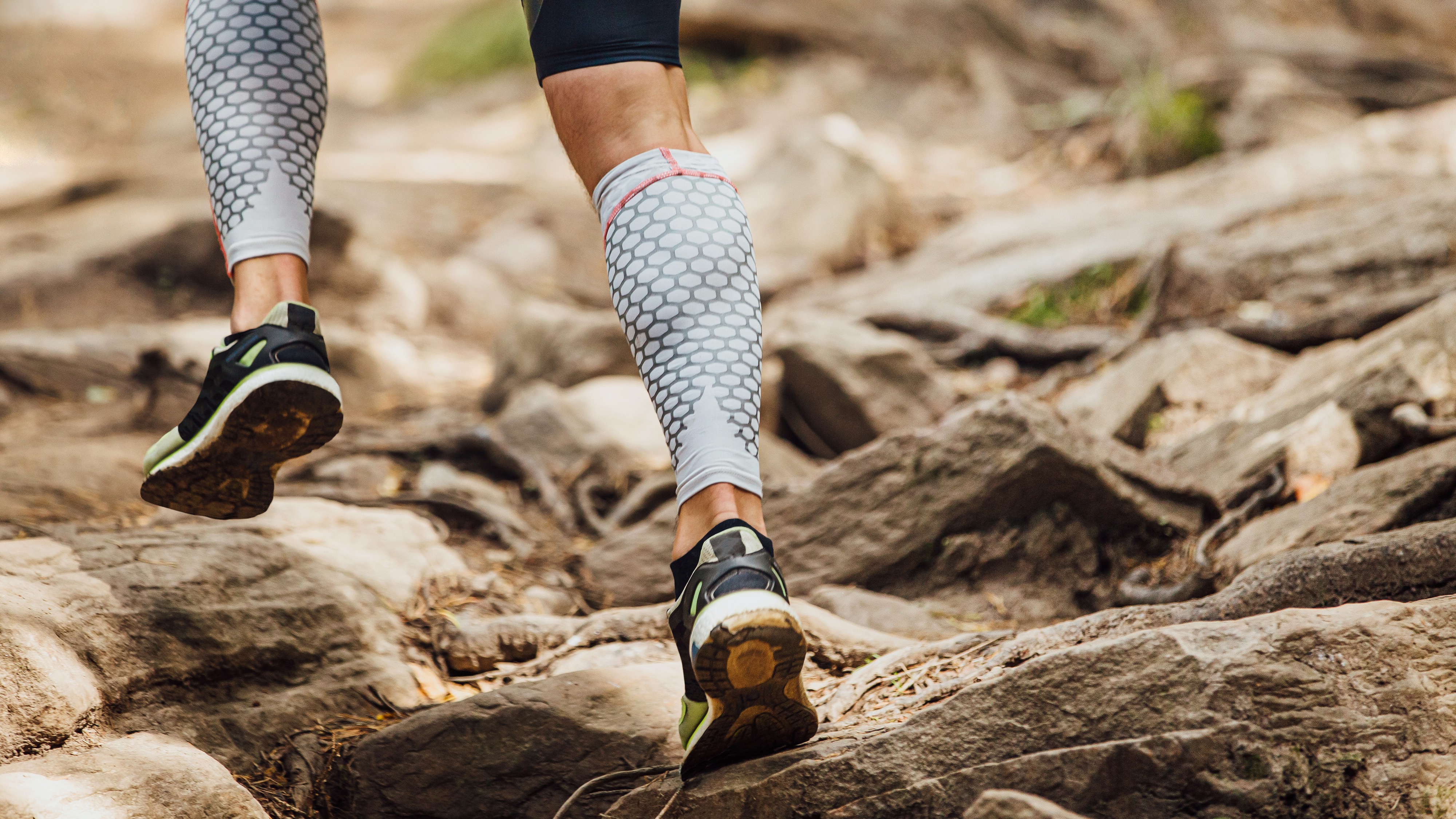 A person wearing running shoes and compression tights running over rocks