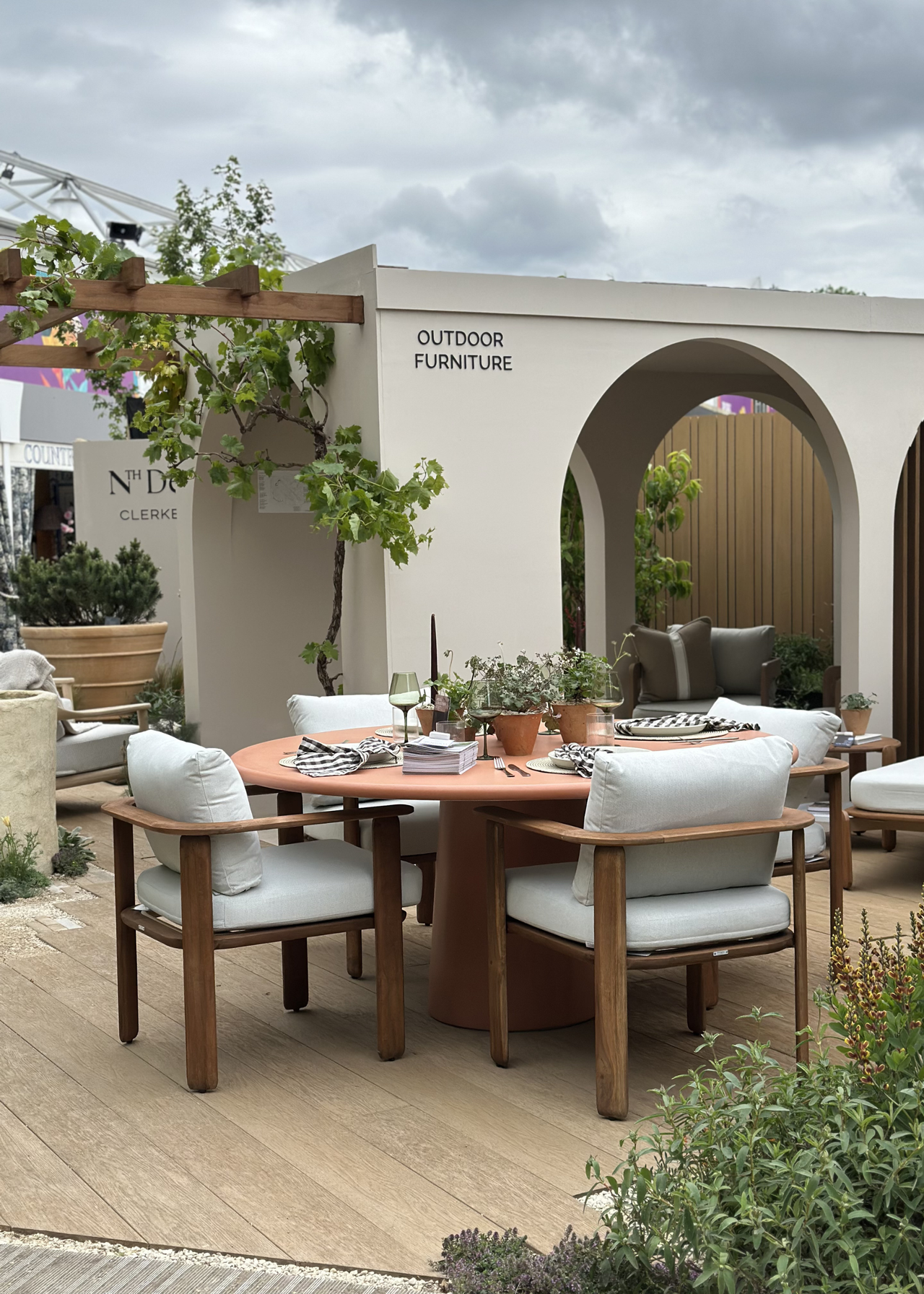 An outdoor dining room styled by Nth Degree with wood armchairs, a round orange dining table, terracotta pots, and candlesticks