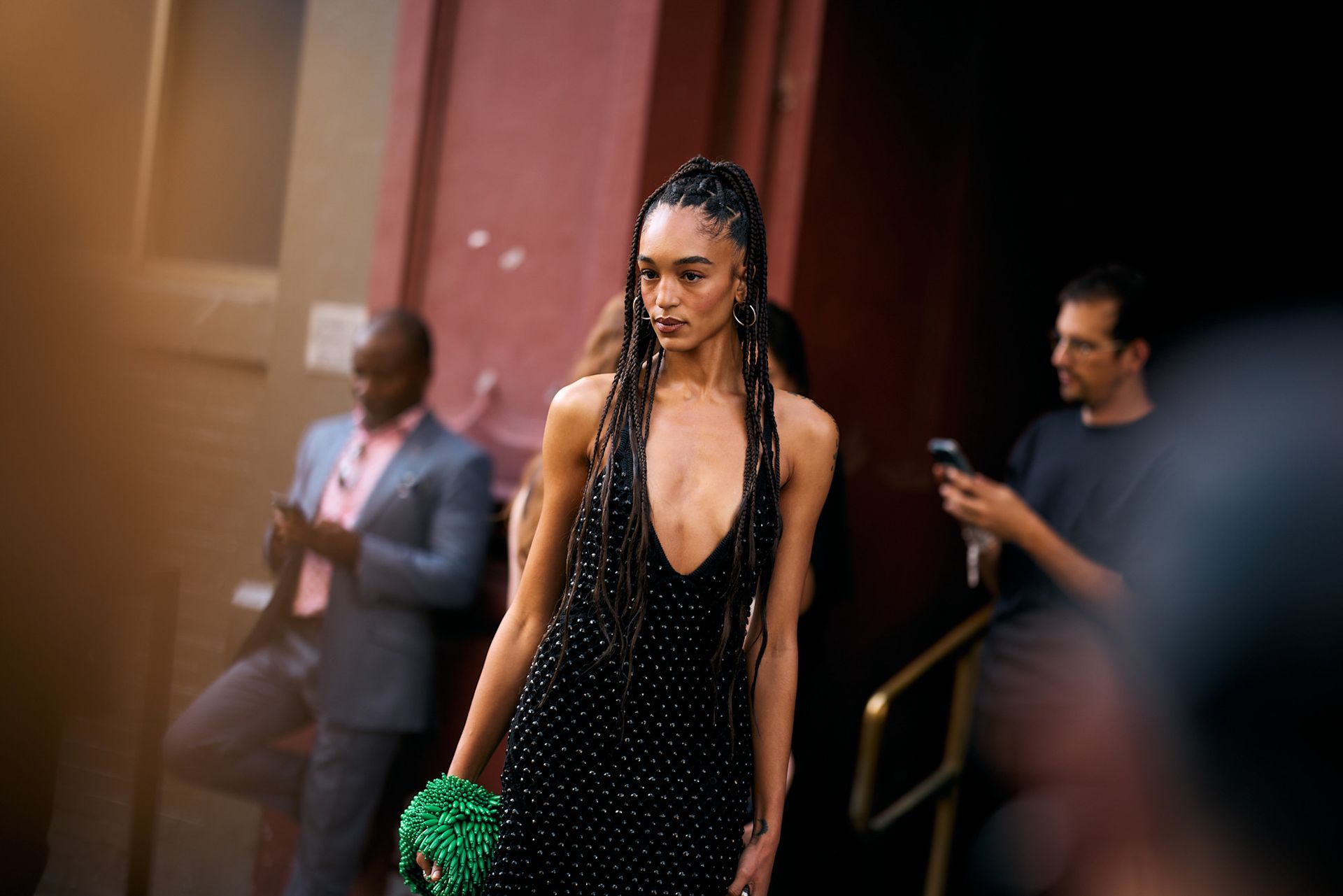 a black woman with braids in a half-up, half-down style with a black dress and green bag
