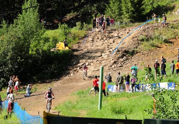 Riders descend a rock garden while spectators watch
