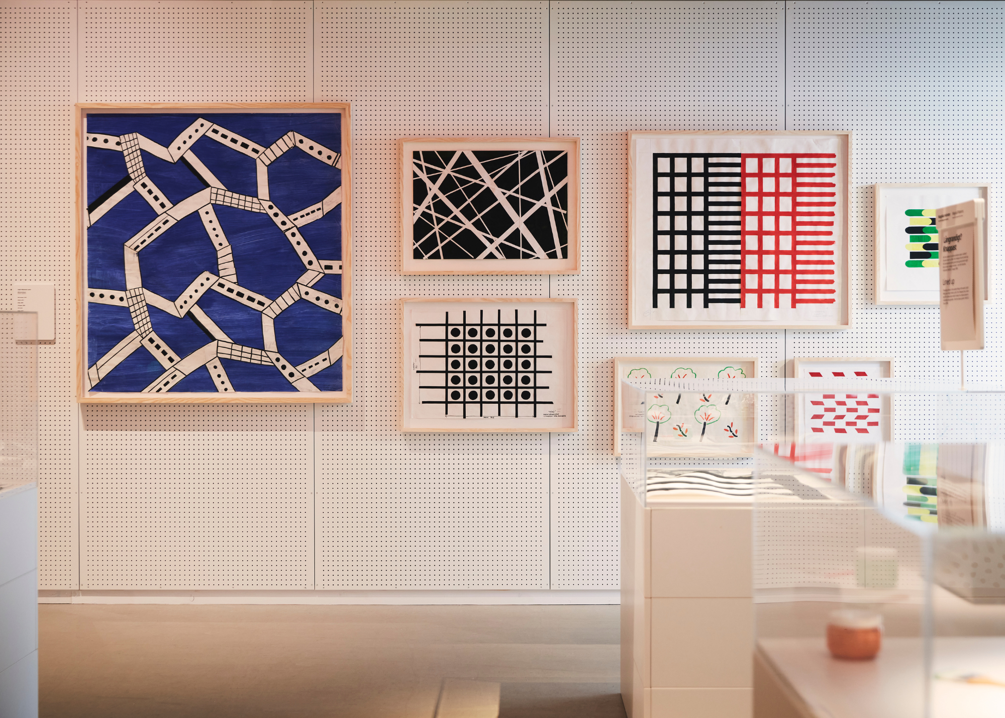 A dotted wall with wood framed textiles including a blue print, two black and white geometric prints and a black and red graphical pattern