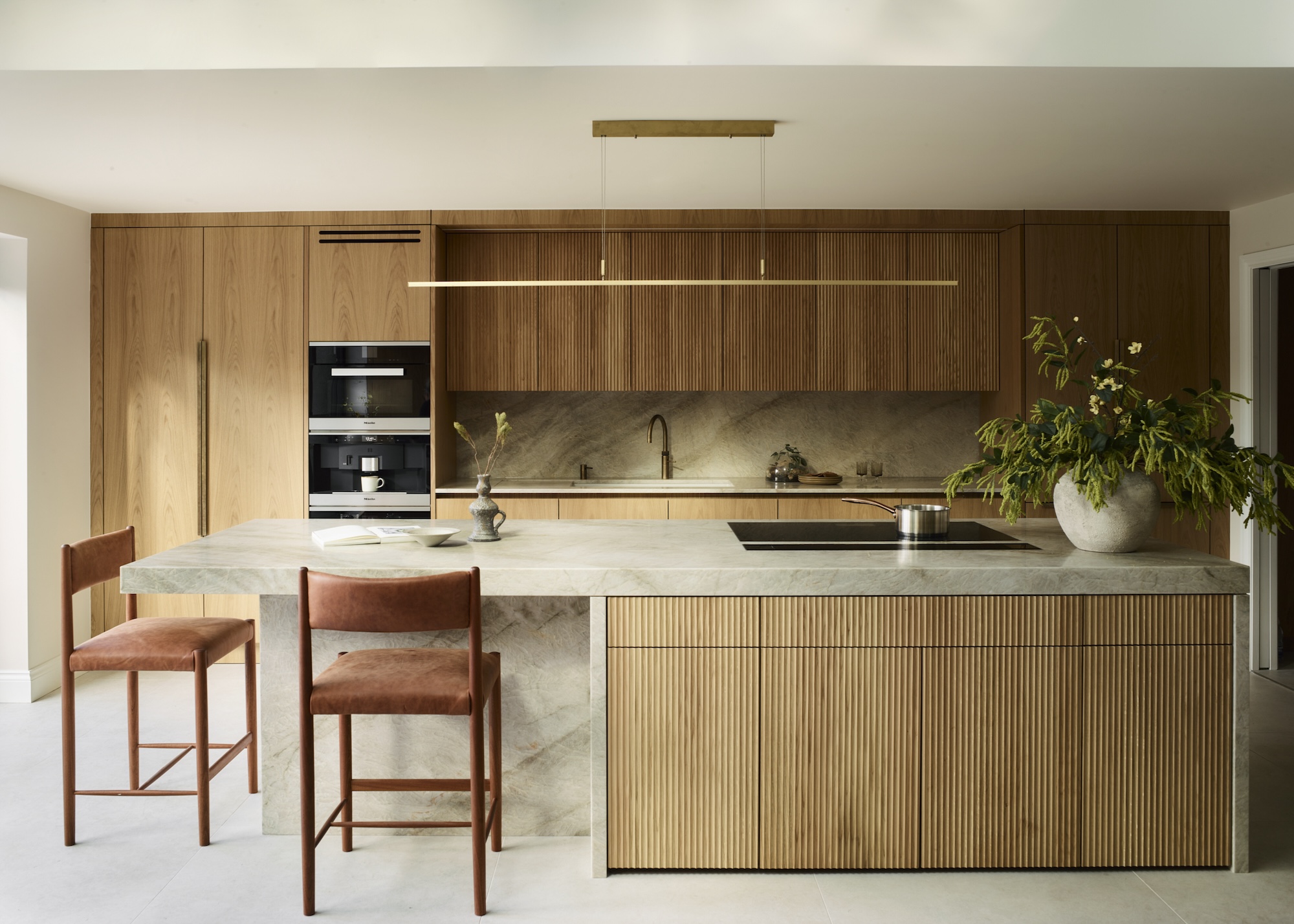 A modern, pared back kitchen in light timber with fluted wall cabinets echoed by fluted door fronts on the island unit