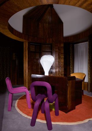 Office room, purple bespoke chairs, dark wood desk on a round burnt orange rug, white balloon shaped feature lamp, dark wood room surround, wooden circular feature on the ceiling, grey scale floor