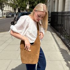 Woman wears white blouse, blue jeans and brown suede crossbody bag