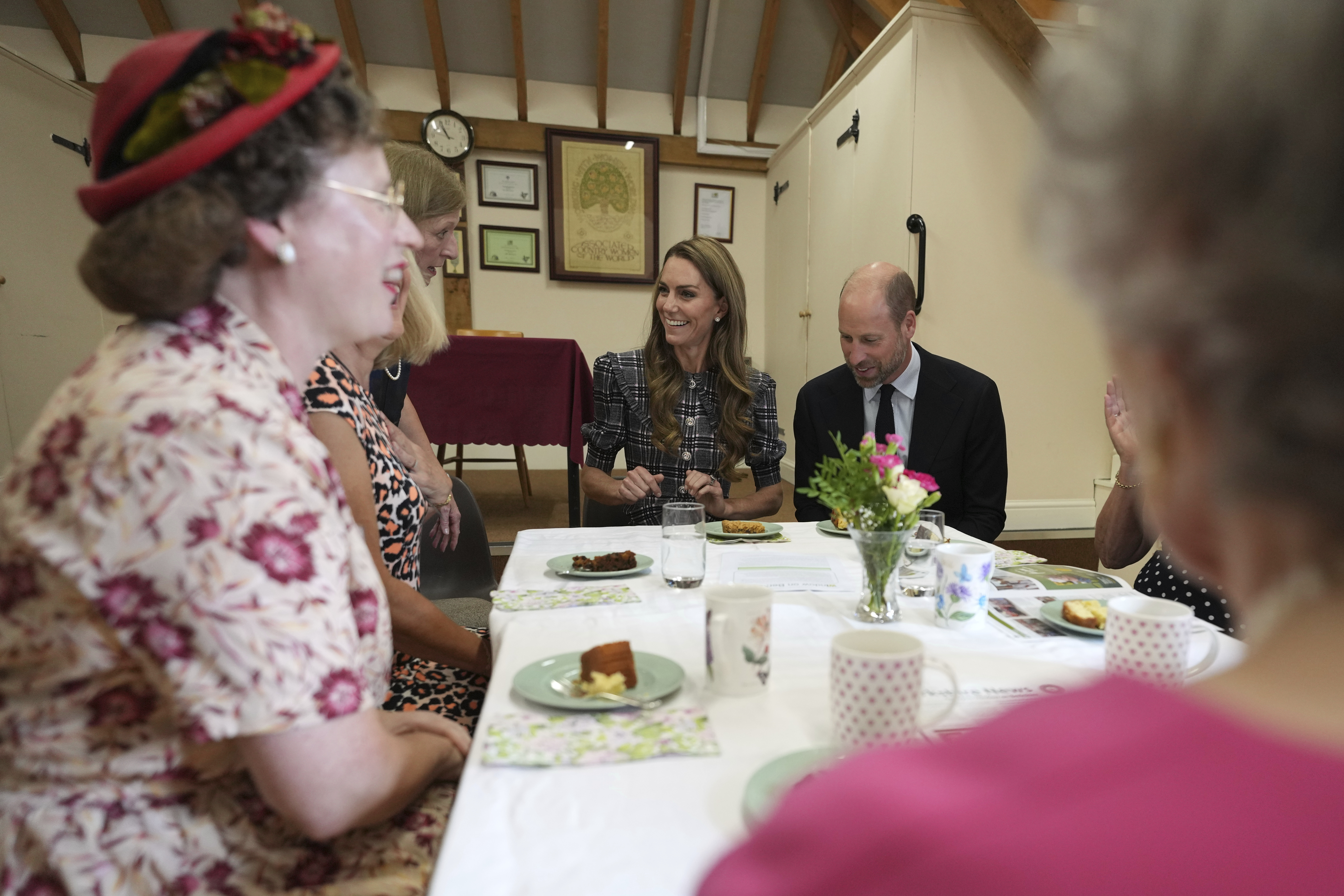 Prince William and Princess Kate sitting at a table of women eating cake