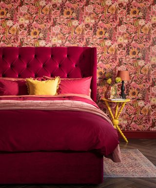 A rich toned red bedroom with a berry red bed frame and patterend wall paper, a yellow cushion on the bed