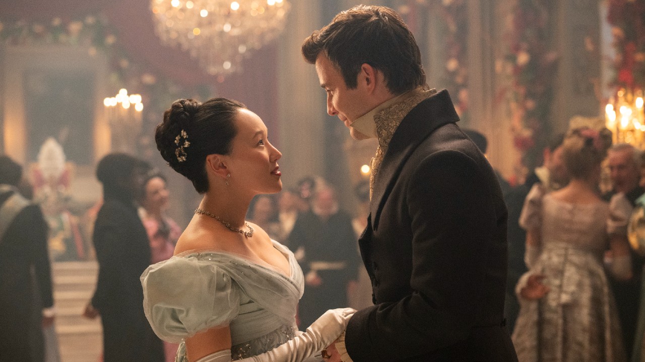 Sophie and Benedict facing each other at a ball and holding hands. 