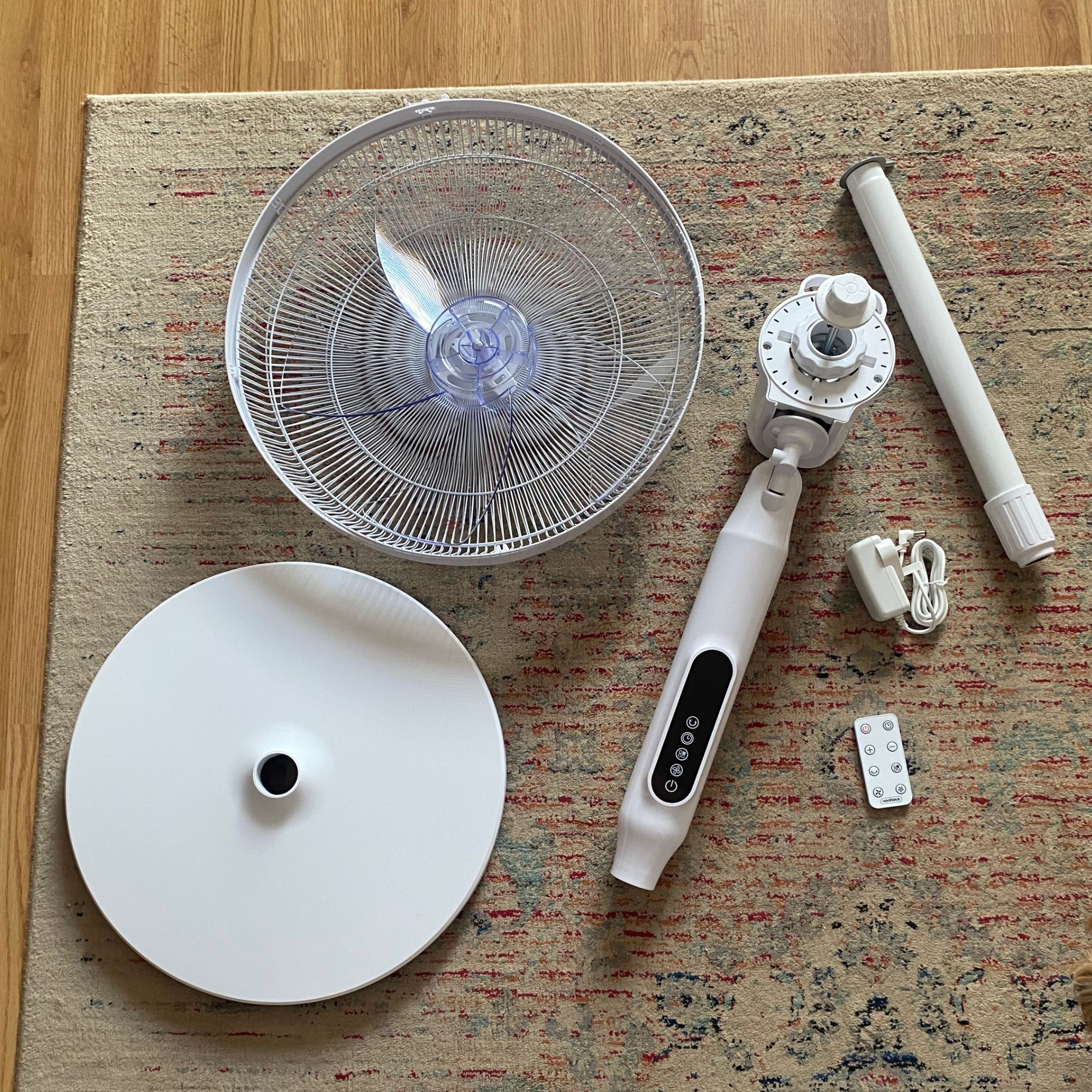 Flat lay of the parts you get in the box when you buy the Vonhaus 16'' pedestal fan, including the base, fan motor, grill and blades, pole, charger and remote control