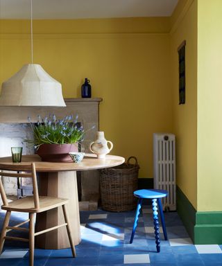 Yellow dining room with green skirting, blue tiled floor, round wooden dining table, low hanging white pendant