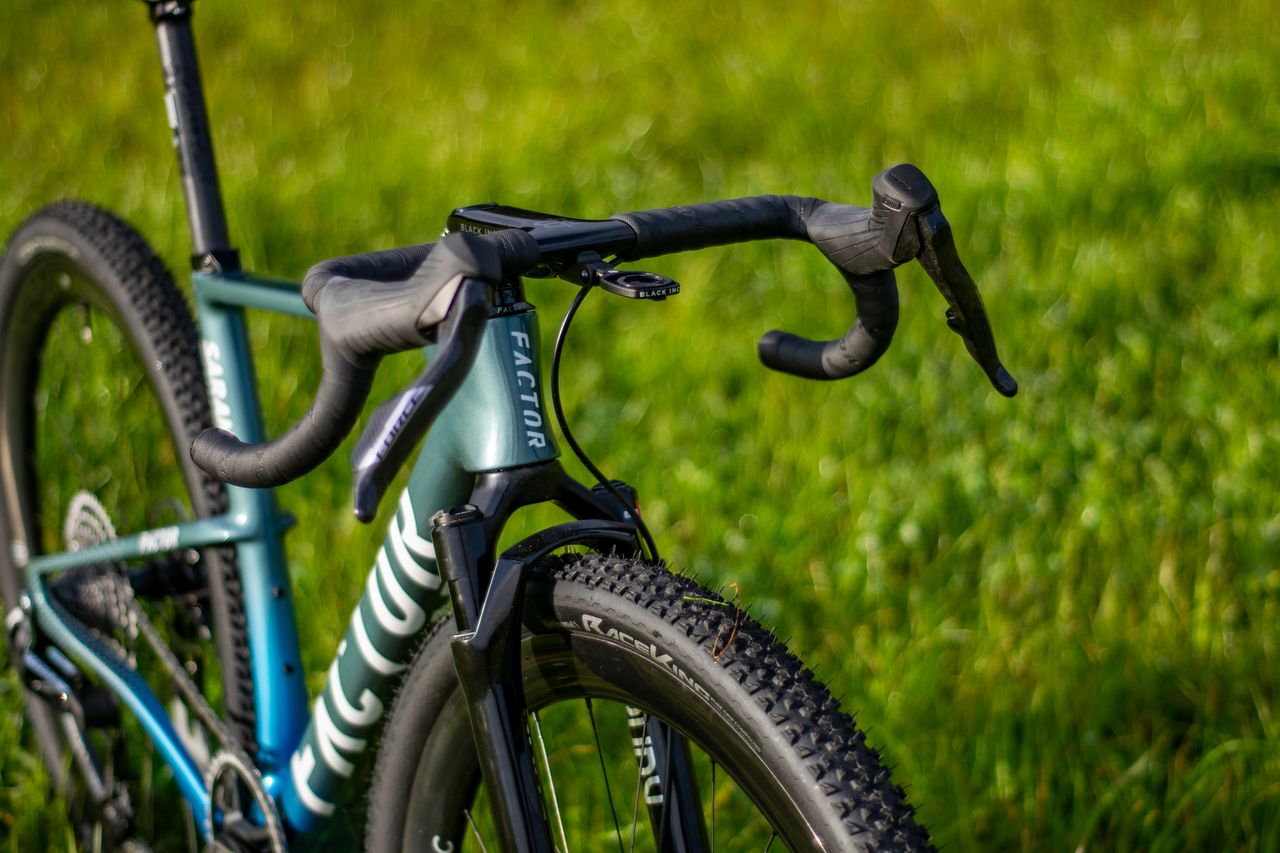 A blue Factor Sarana gravel bike in a grassy field with a hedge in the background