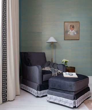 A green bedroom with a black armchair and square ottoman