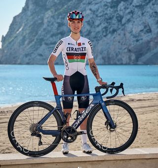 Fariba Hashimi standing in front of the beach with her Orbea team bike