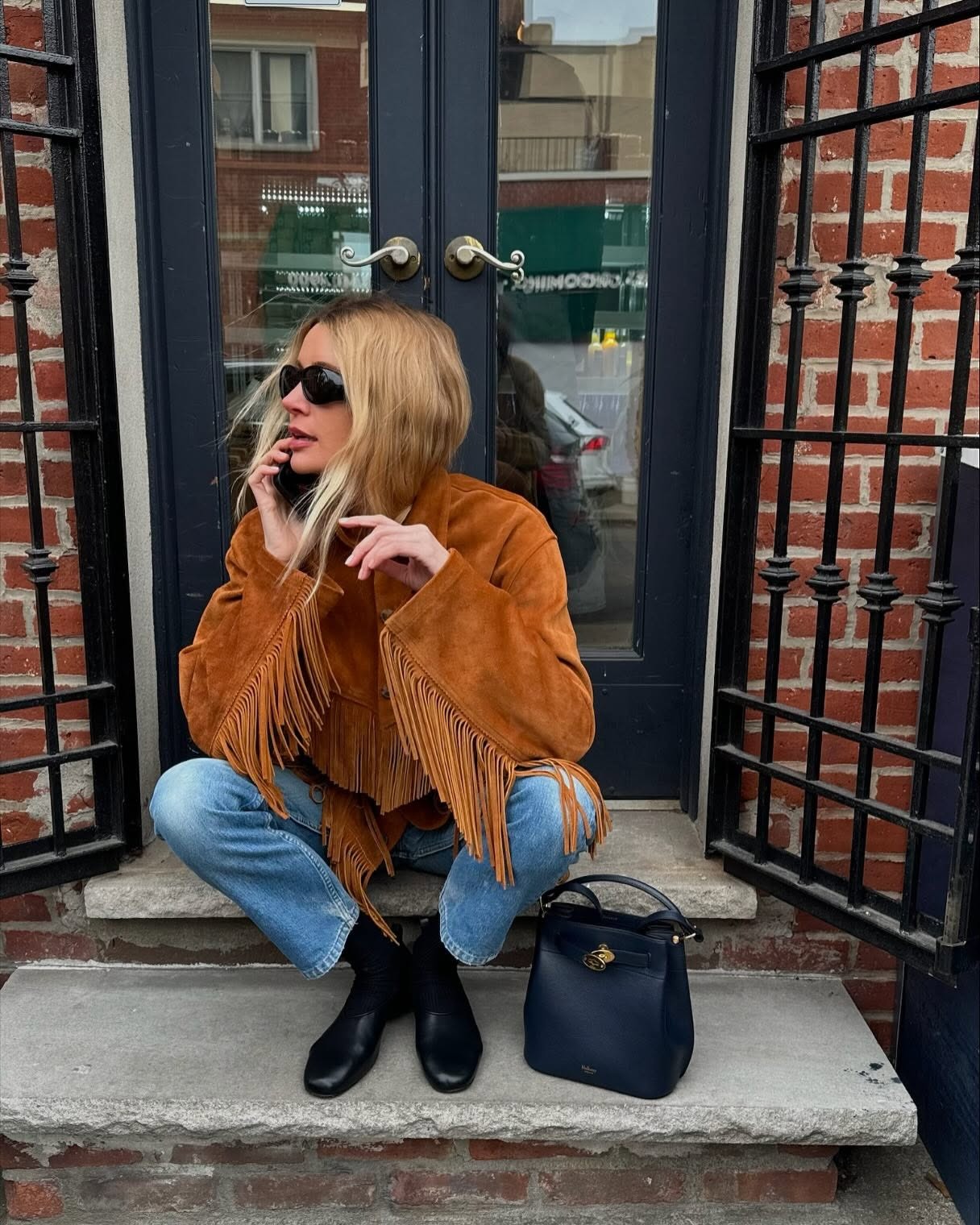 Courtney Grow wears a brown suede fringed jacket with jeans and flats on a New York city stoop.