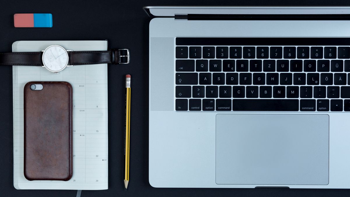 A laptop, phone, watch and notepad all organised neatly on a desk