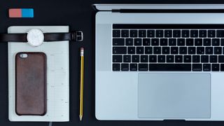 A laptop, phone, watch and notepad all organised neatly on a desk