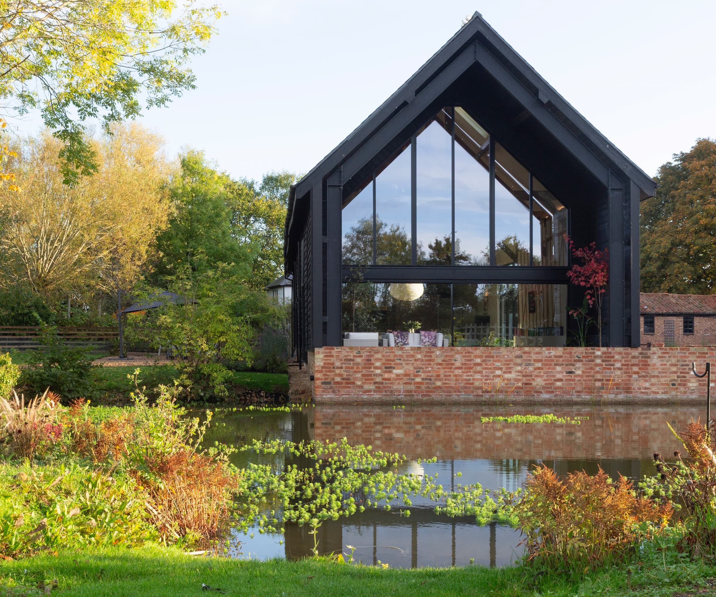 A barn next to a river with a brick wall with a tall glass front and black cladding