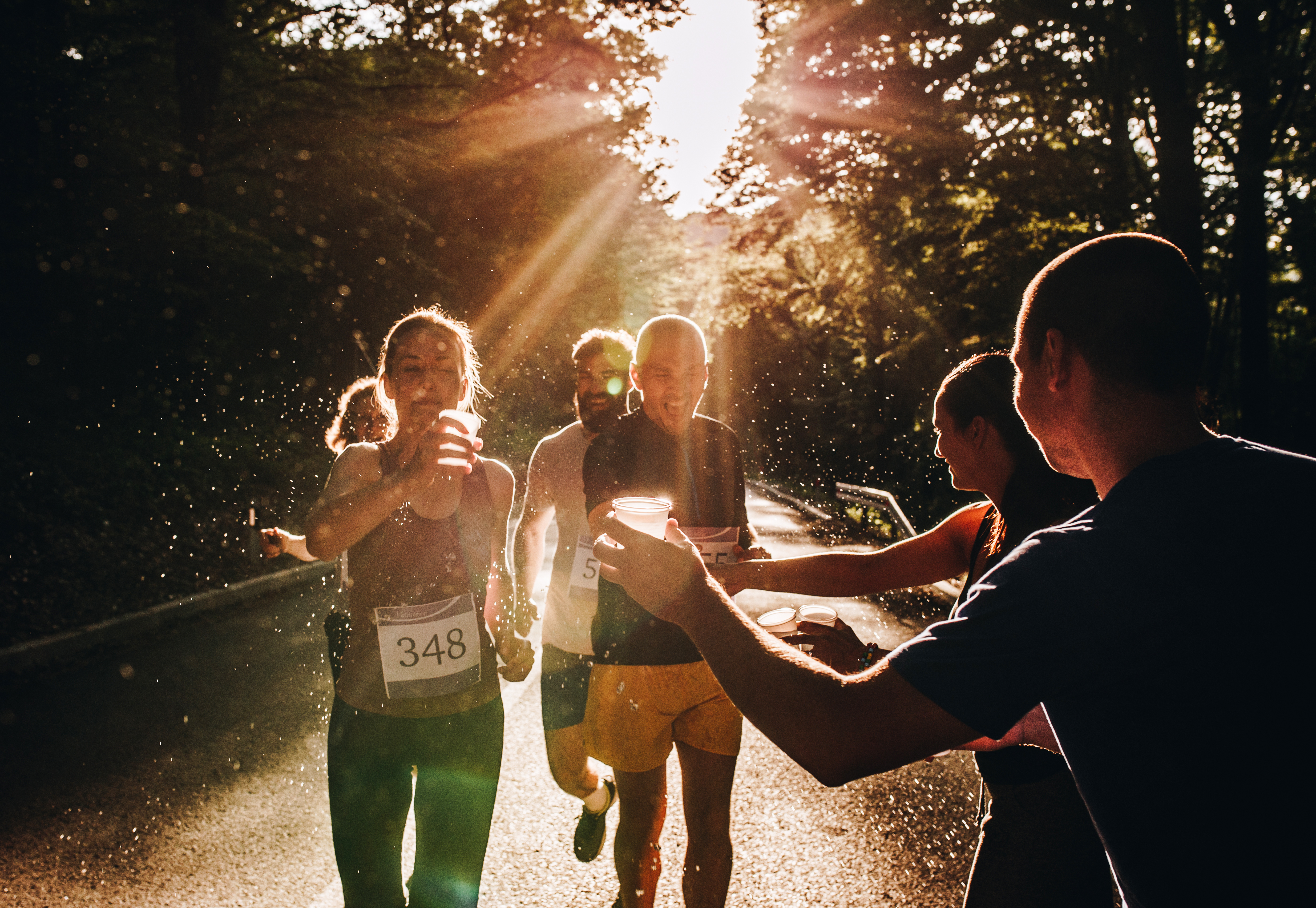 an image of runners getting water from volunteers during a marathon at sunset