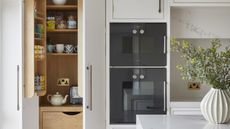 A kitchen with a double oven, white countertops, and an open pantry with organized shelves 