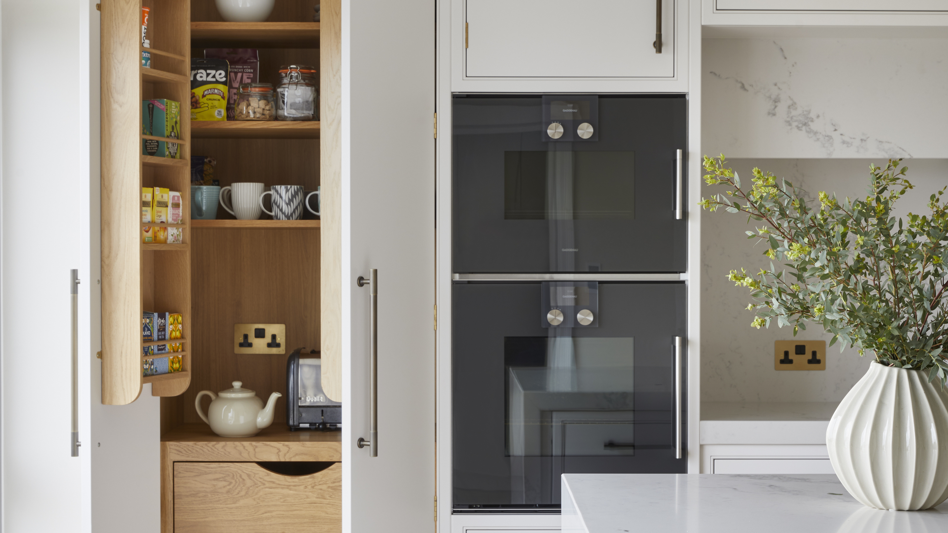 A kitchen with a double oven, white countertops, and an open pantry with organized shelves 