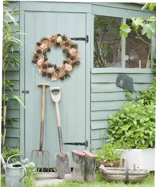 Soothing sage painted shed with rustic wreath on door, and leaning long handled gardening tools.