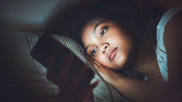 Women lies awake in bed scrolling on her phone