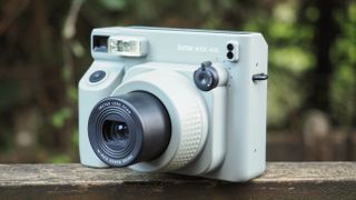 An Instax Wide 400 camera, on a wooden surface in a woodland setting