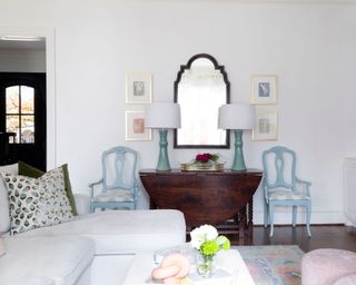 Living room with white sectional and two blue chairs flanking side table with table lamps and mirror above