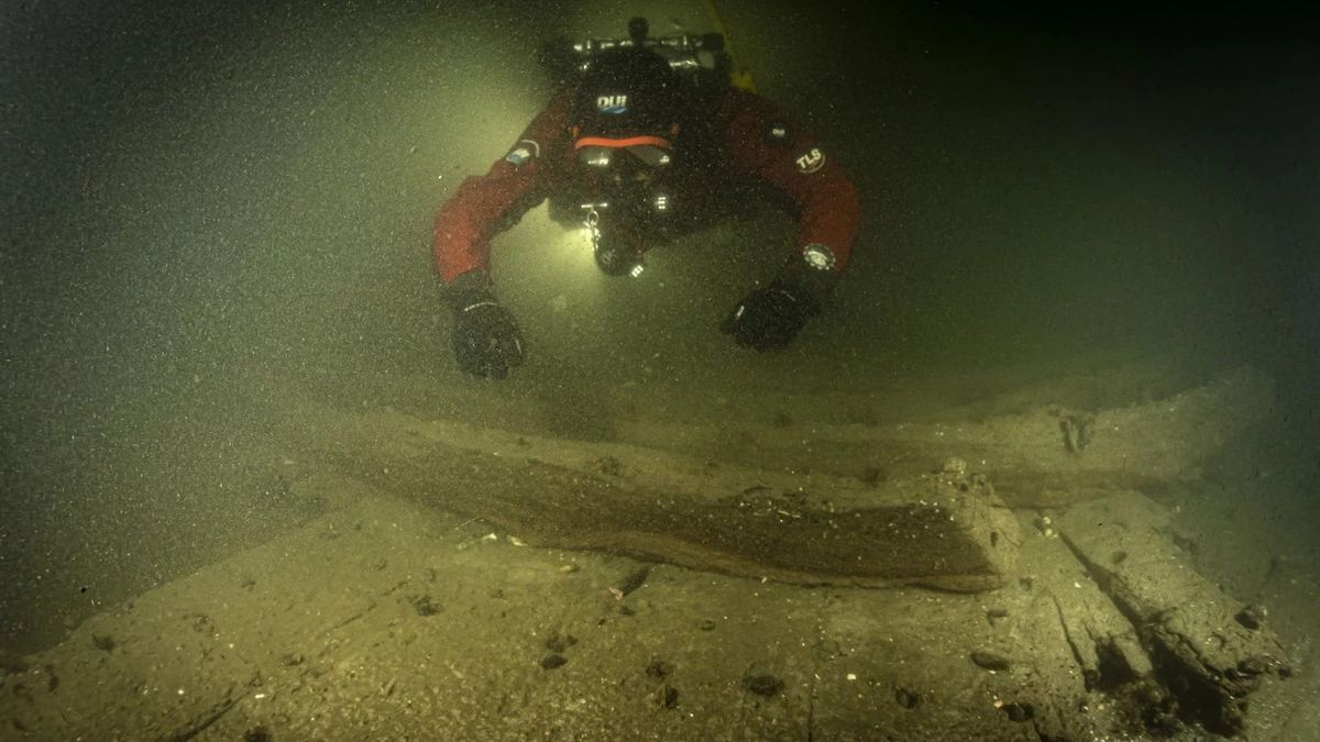 A scuba diver in deep dark water inspecting a sunken vessel.