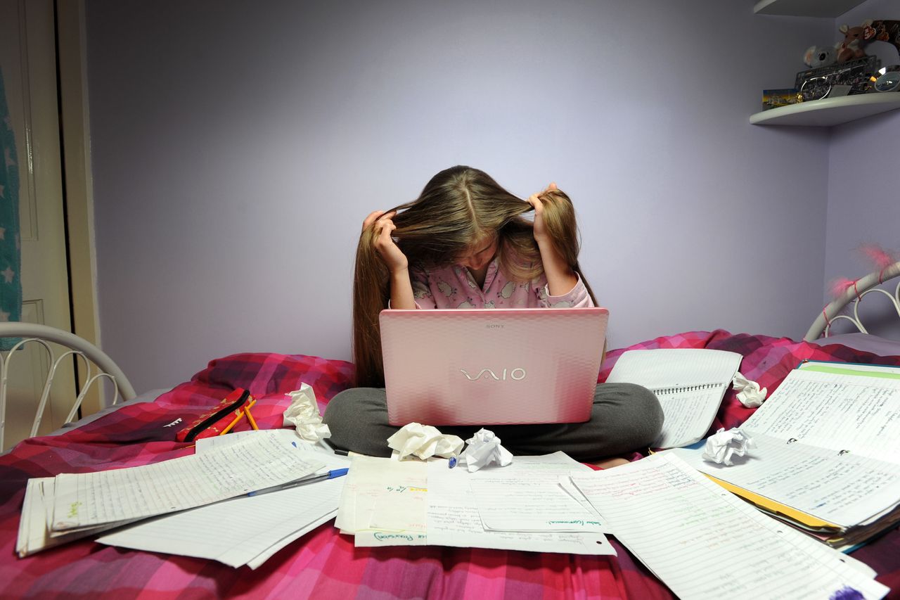 Teenage girl stressed studying with laptop on bed