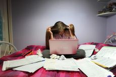Teenage girl stressed studying with laptop on bed