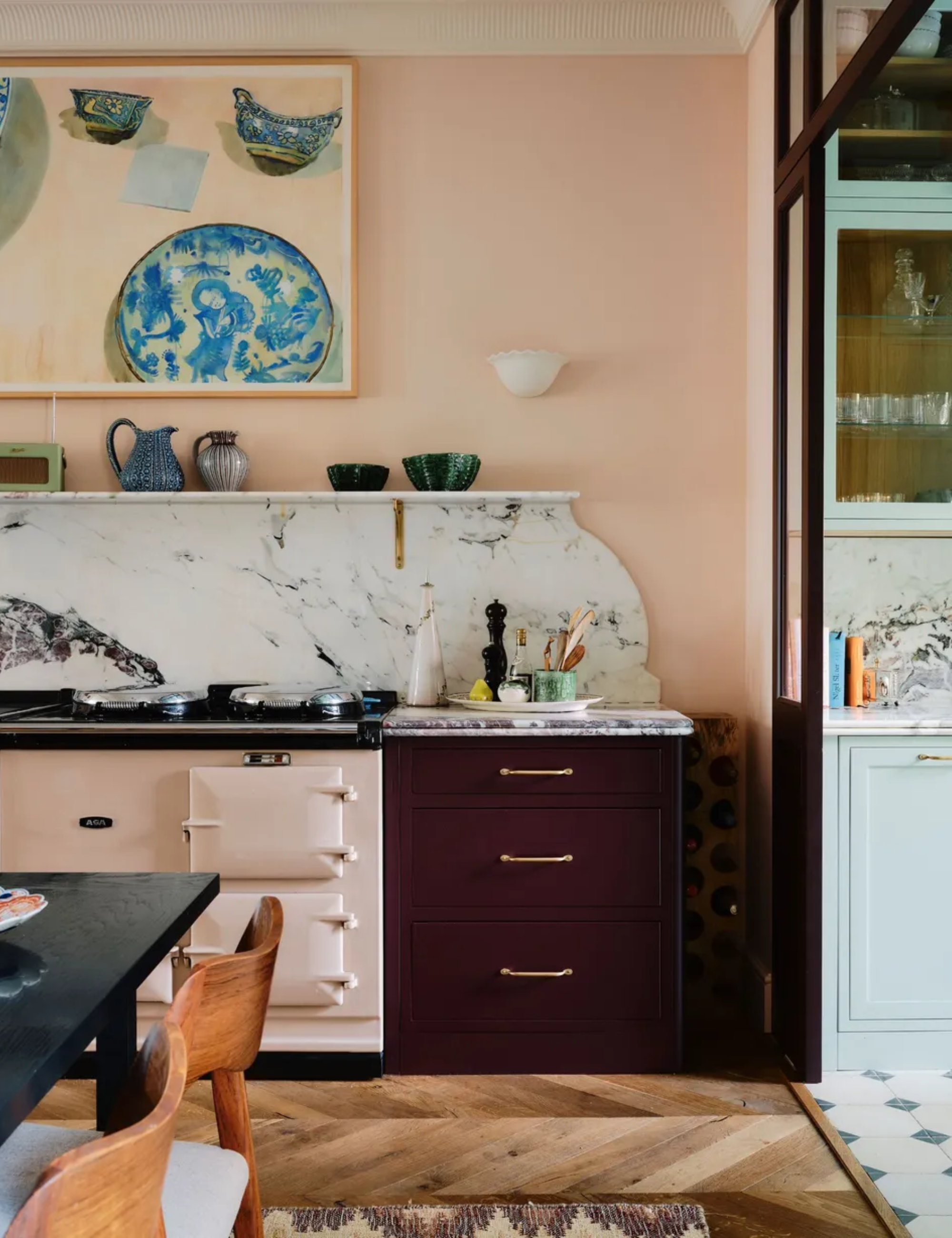 pale pink painted kitchen with dark red cabinetry, statement marble backsplash, an Aga, and a large painting hung on the wall