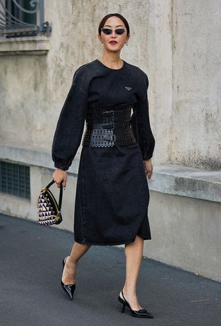 One of the best designer belts is shown in a close street-style photo of a woman wearing a gray Prada dress with black slingback heels and an Alaïa corset belt