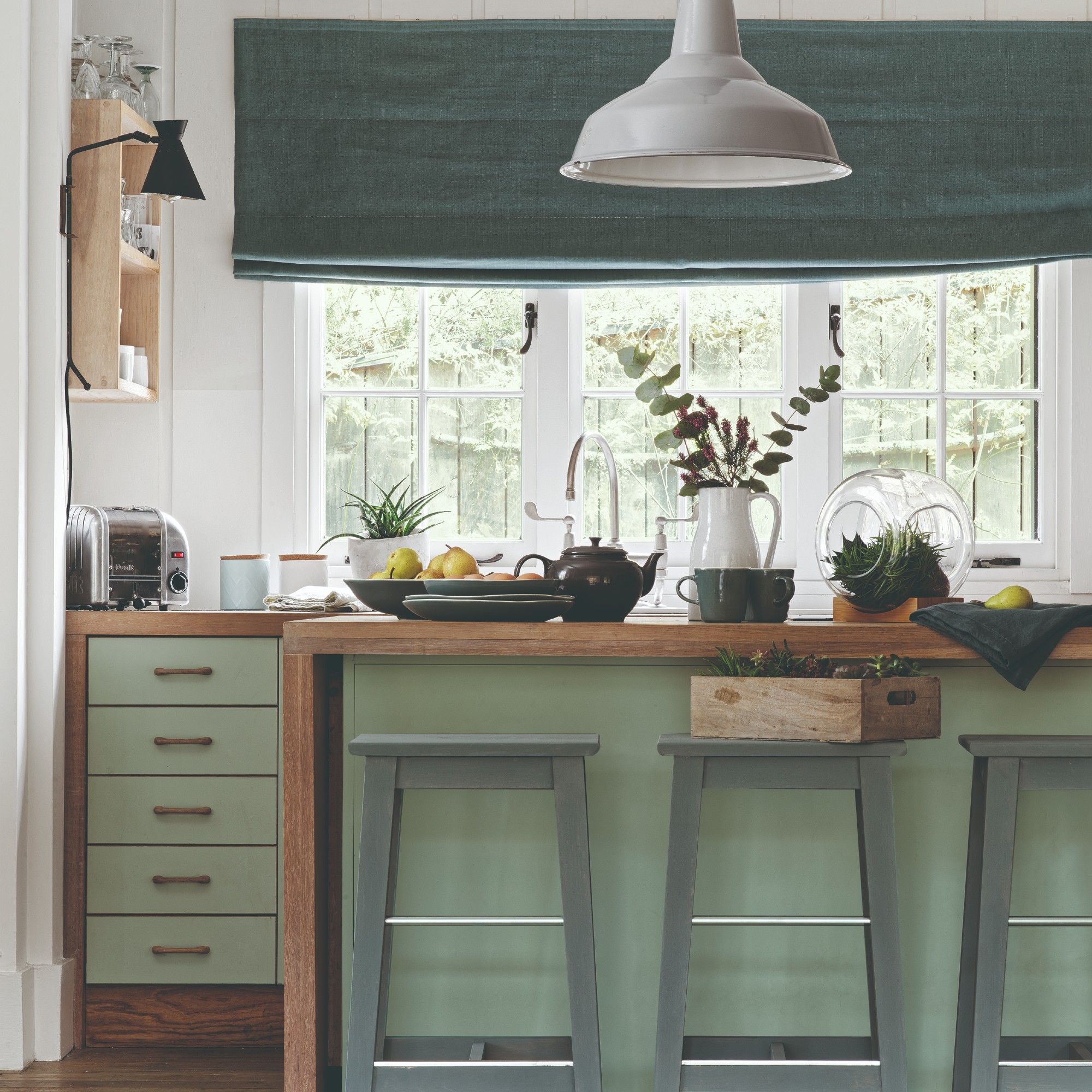 Green and wood kitchen with white pendant light over the kitchen island and a green blind over the window