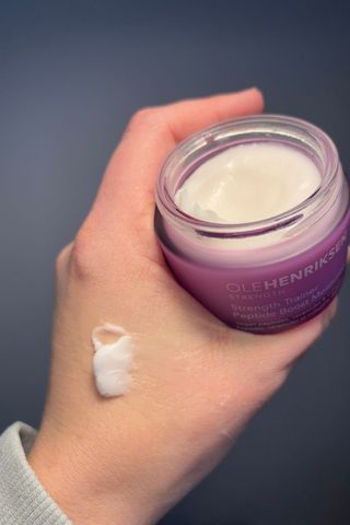 a hand holding ole henriksen strength trainer peptide moisturizer with a smear of cream