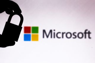 Microsoft logo on a white background with a sihlouette of a hand holding a padlock in the foreground denoting security