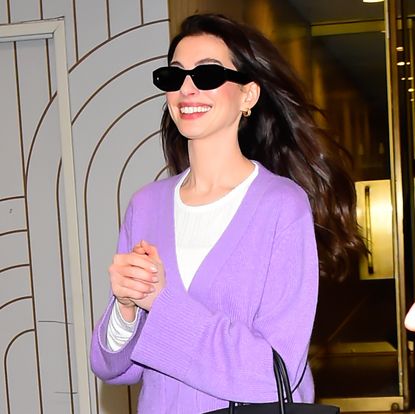 Anne Hathaway in chunky sneakers, purple cardigan, white pants, and a Birkin bag.