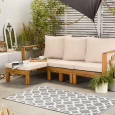 Aldi acacia day bed on a patio with a geometric rug and potted plants.