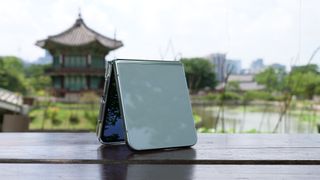 Samsung Galaxy Z Flip 5 resting on a bench with a pond and a Korean pagoda behind it 
