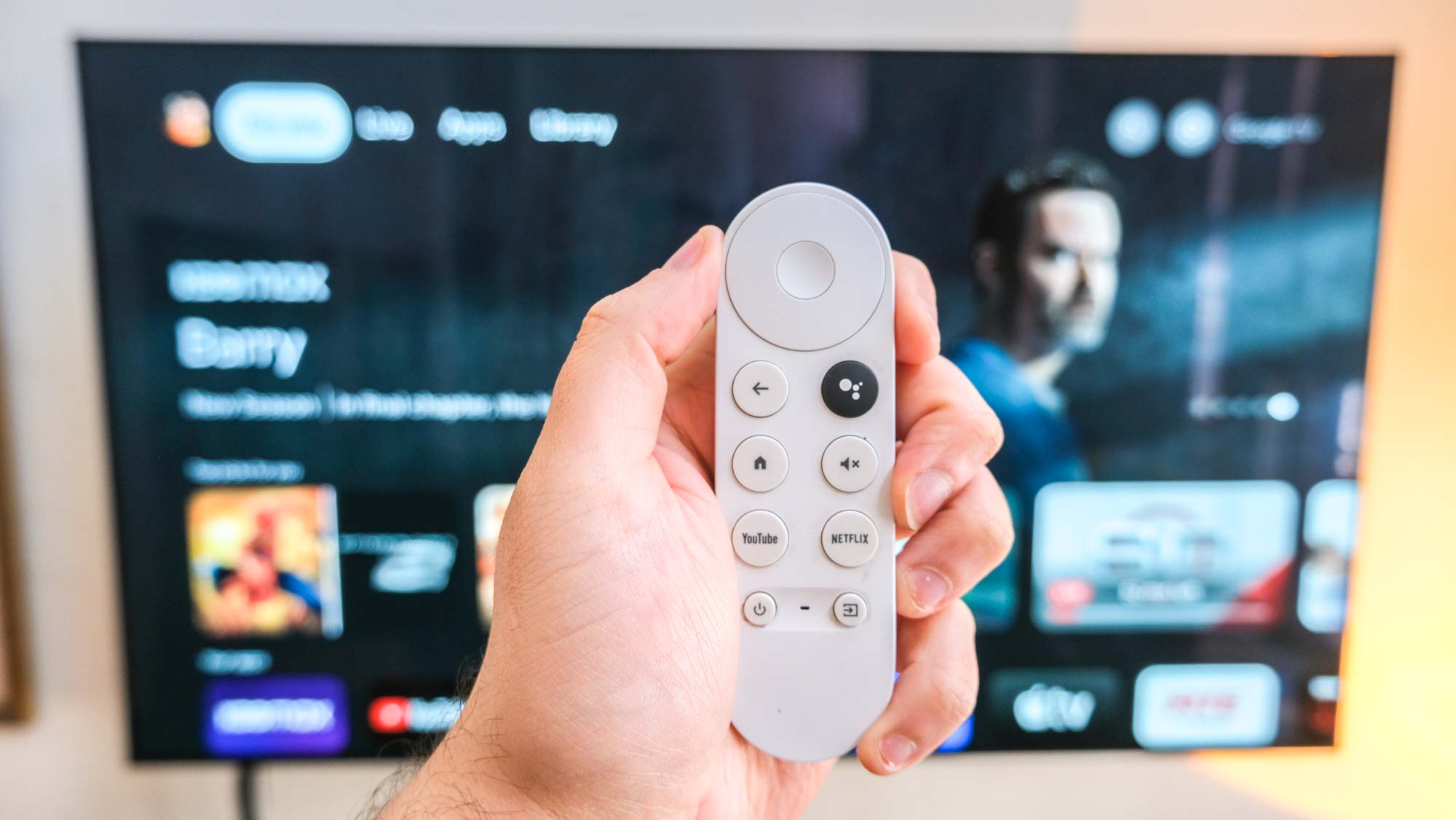 Der Chromecast mit der Google TV-Fernbedienung vor einem Fernseher, auf dem eine Barry-Werbung zu sehen ist