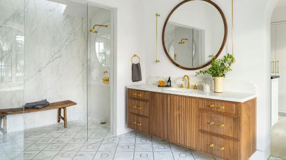 bathroom with wood vanity and marble top, round mirror and marble shower