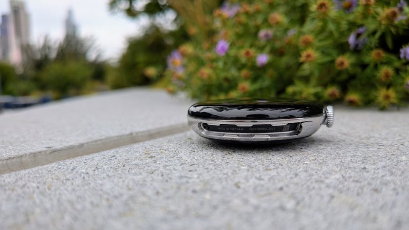 A photo of the Google Pixel Watch 4 45mm case with bands removed, upside down, sitting on a concrete area with plants behind it.