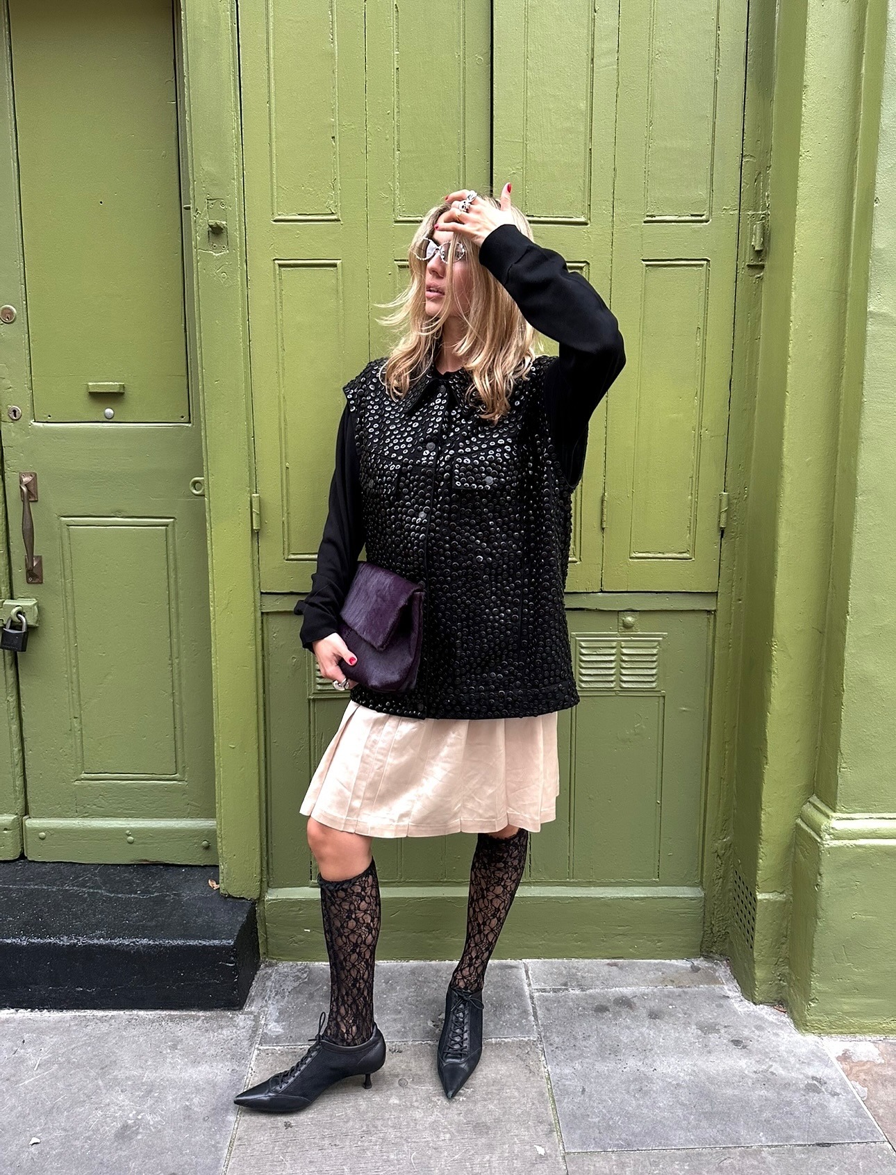 Fashion person Torivan Breugel wears black lace knee-high socks. She pairs them with a black studded jacket, a beige skirt and a kitten heel boot in a recent image from her Instagram.