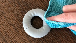 The ear pads of a pair of headphones being cleaned by a blue microfiber cloth