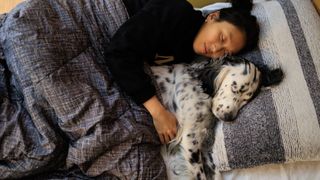 A woman and her dog snuggle up and take a nap