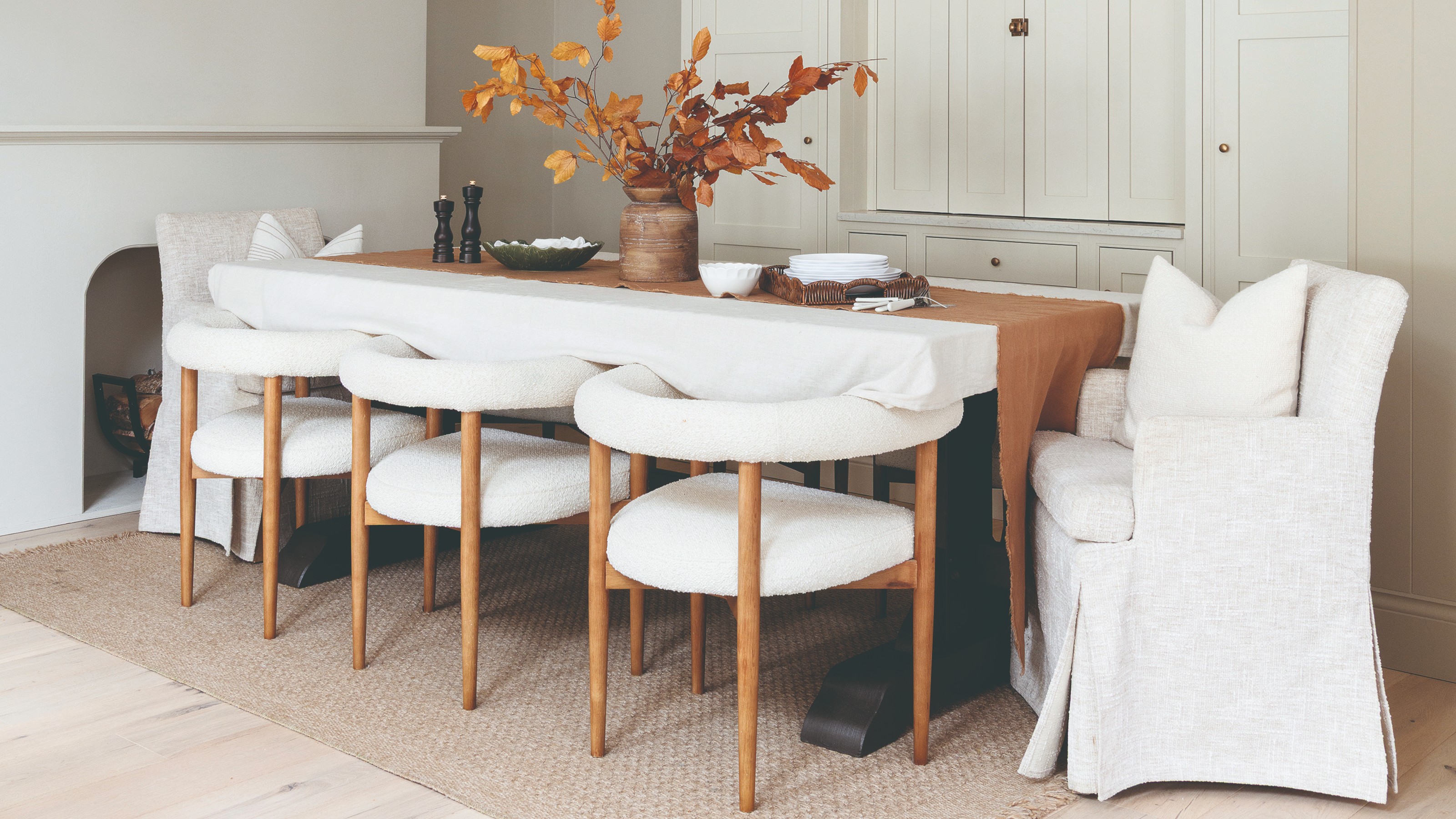 A bright dining area with wooden and white boucle dining chairs and loose-cover armchairs placed at the ends of the table