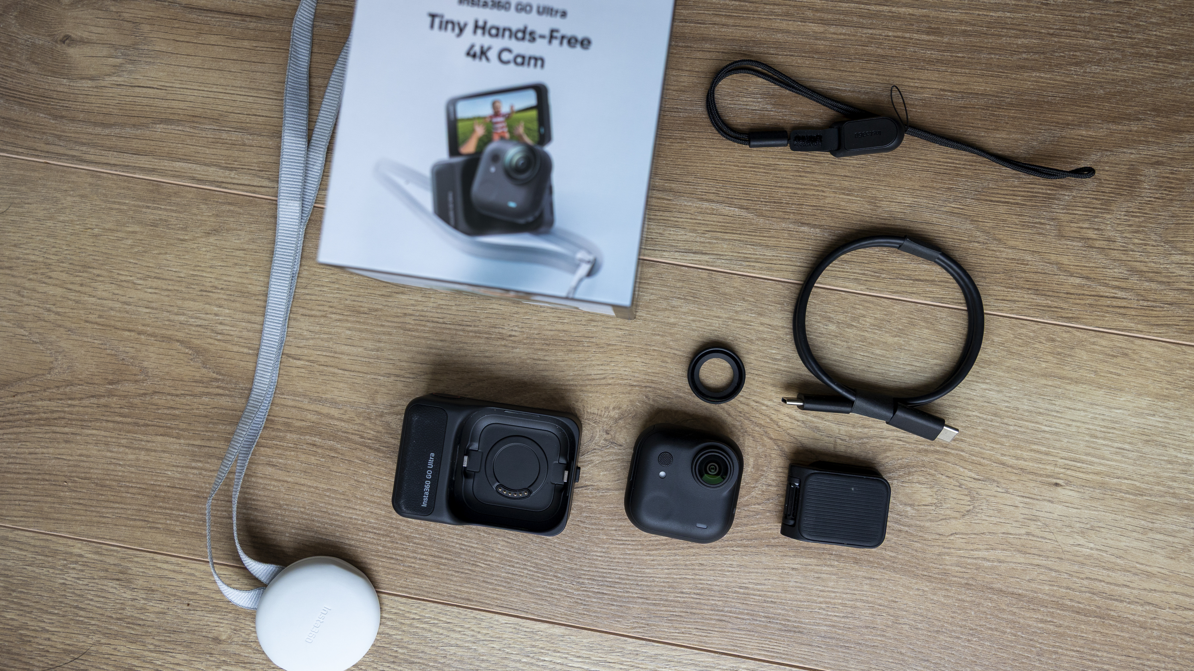 The box contents of the Insta360 GO Ultra including a USB-C and lens protector on a wooden floor