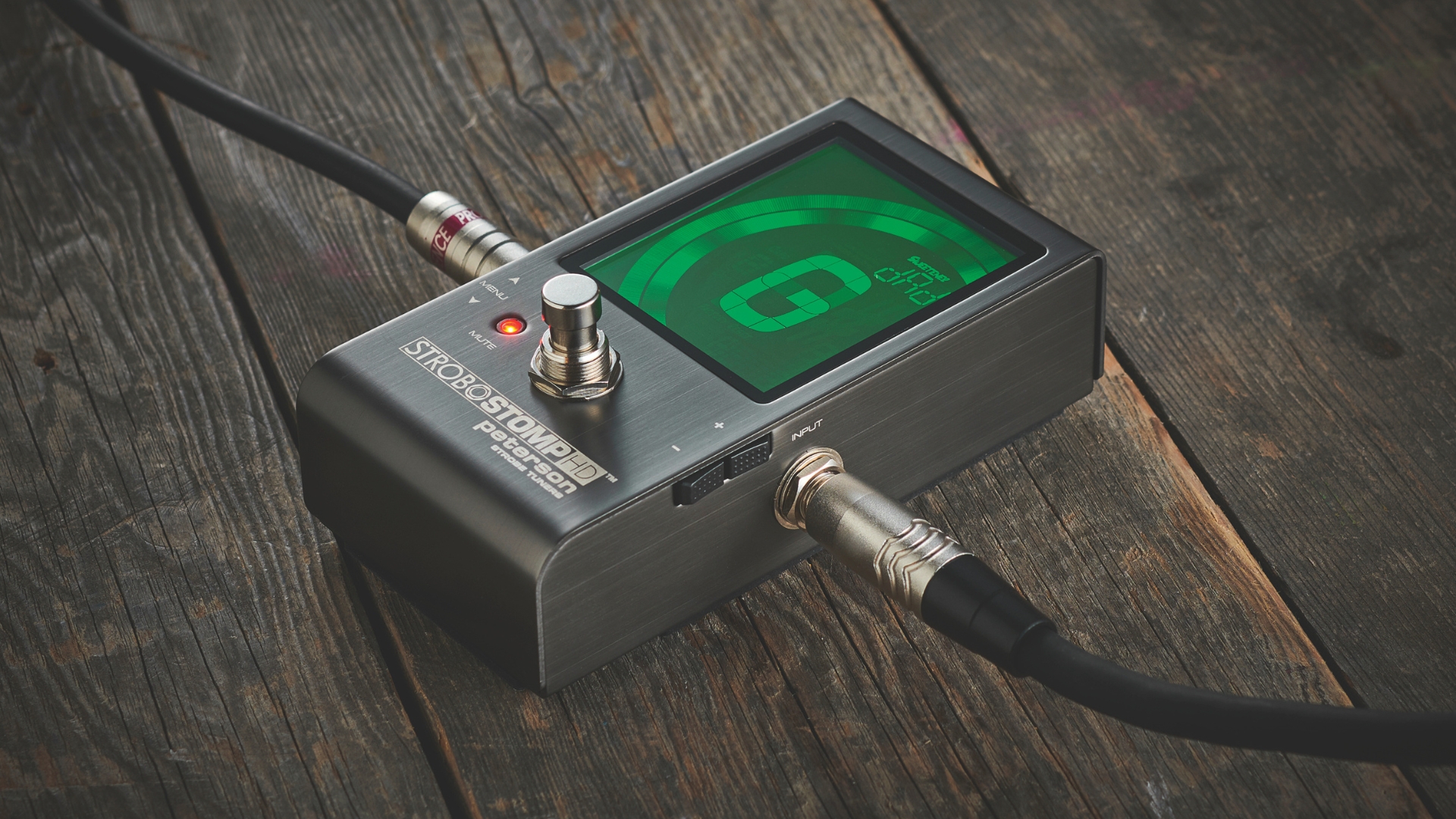 A Peterson StroboStomp guitar tuner lying on a wooden floor