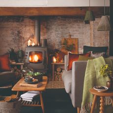 A cottage-style living room with a lit wood burning stove and candles surrounding it, casting a warm glow