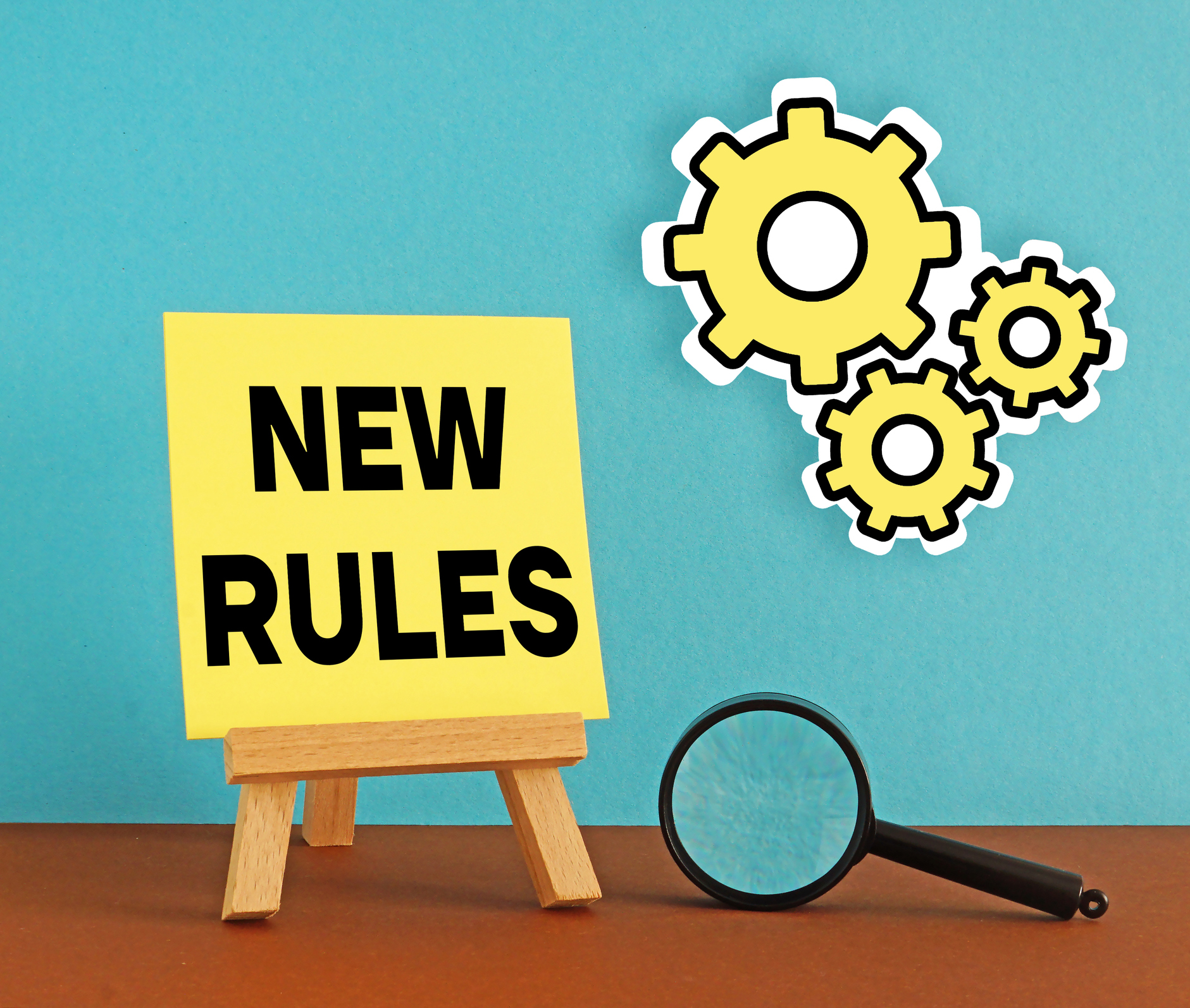 mini easel that says &quot;new rules&quot; with yellow cogs and a magnifying glass