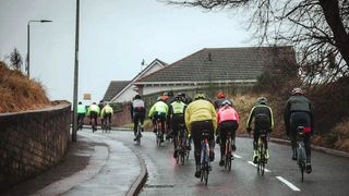 A group of cyclists ride in the rain